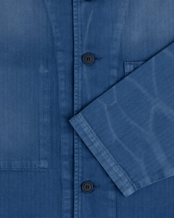 Close-up of the Sun Faded Chore Jacket, a blue button-up with a chest pocket and sleeve crossing the front.
