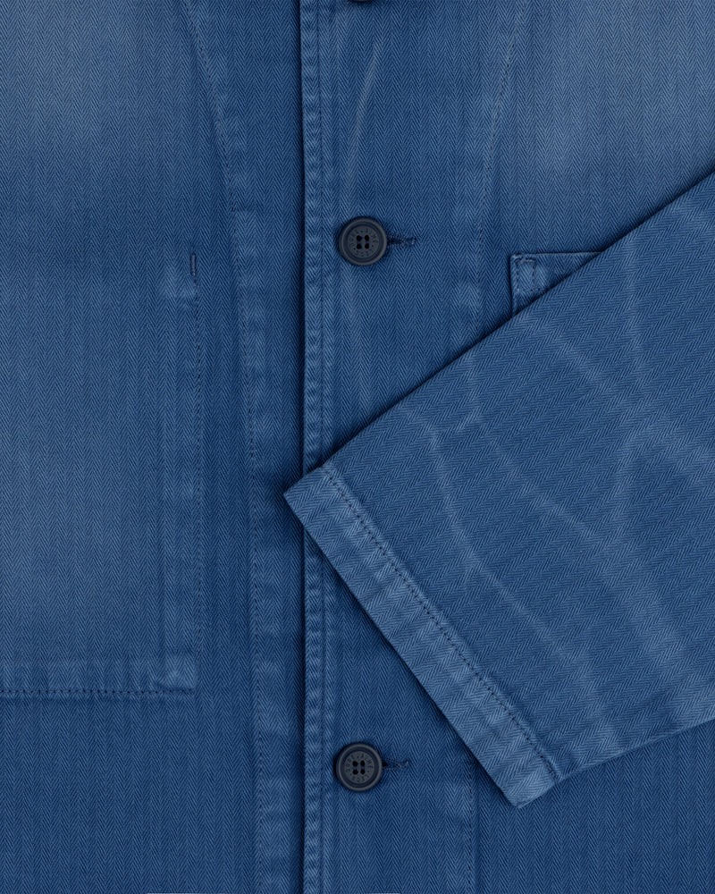 Close-up of the Sun Faded Chore Jacket, a blue button-up with a chest pocket and sleeve crossing the front.