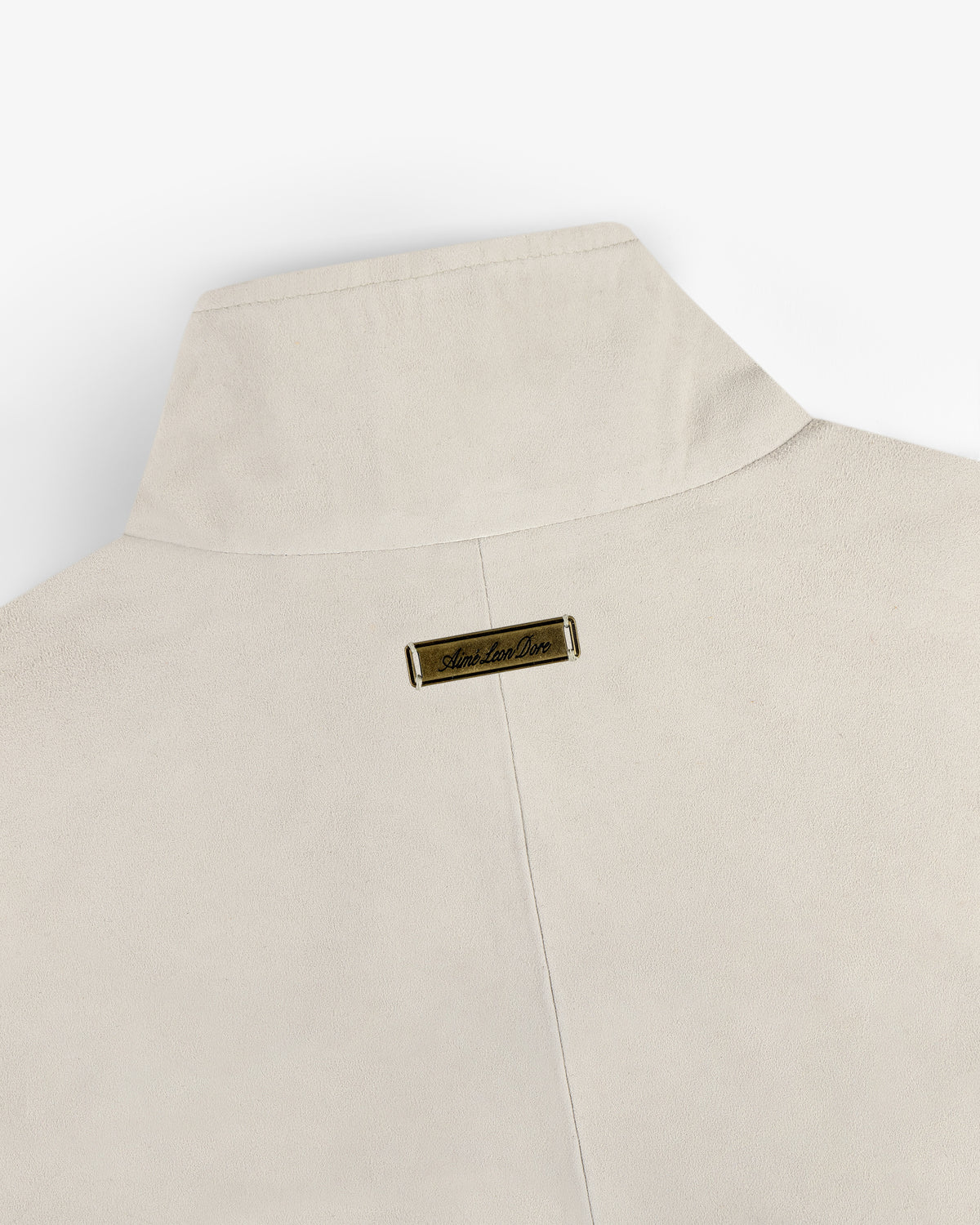 Close-up of the back collar of the Suede Track Jacket in beige with a small gold nameplate near the top center.