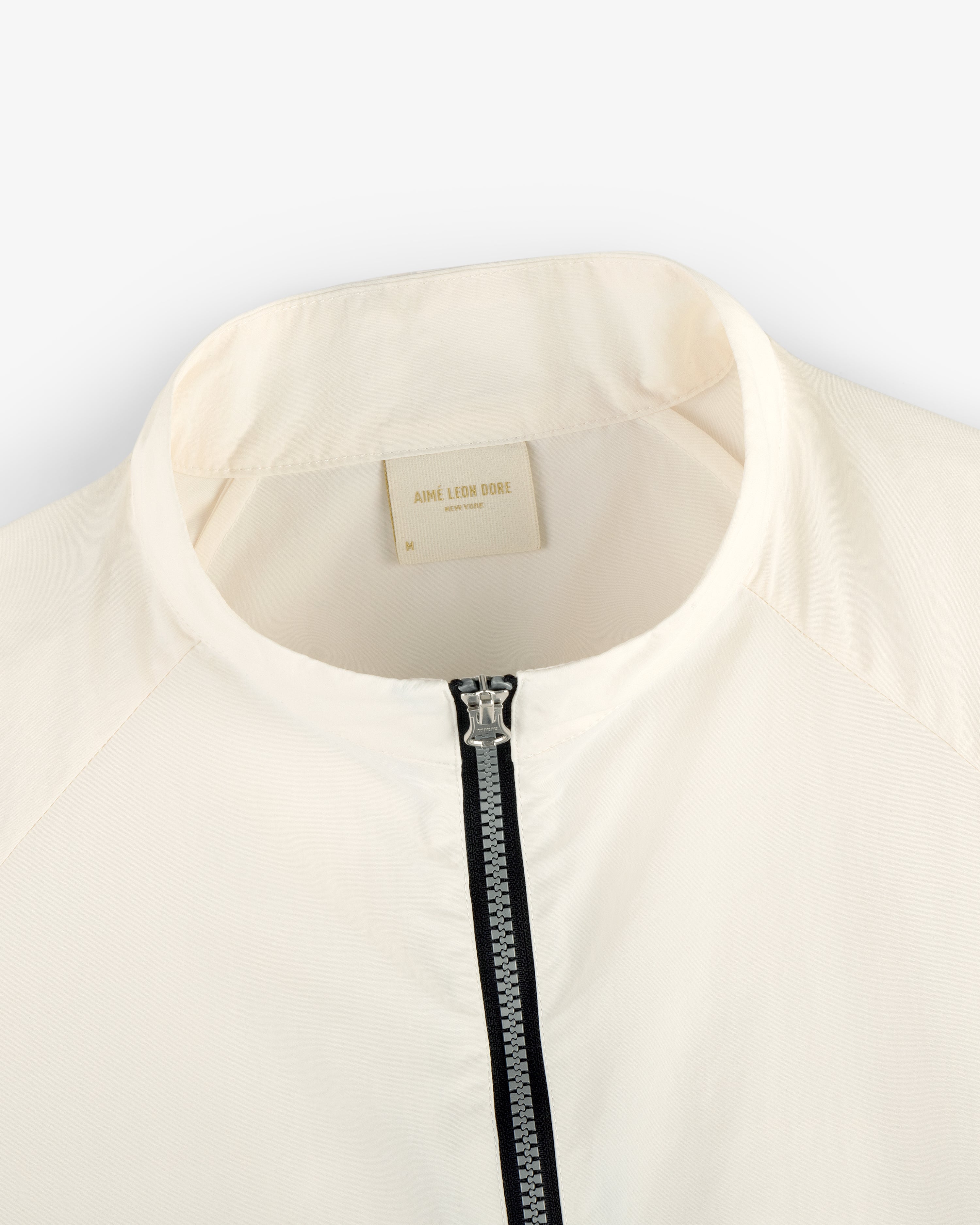 Close-up of the Nylon Packable Windbreaker in cream with a silver zipper and AIMÉ LEON DORE label.
