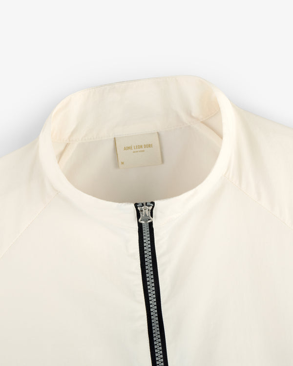 Close-up of the Nylon Packable Windbreaker in cream with a silver zipper and AIMÉ LEON DORE label.