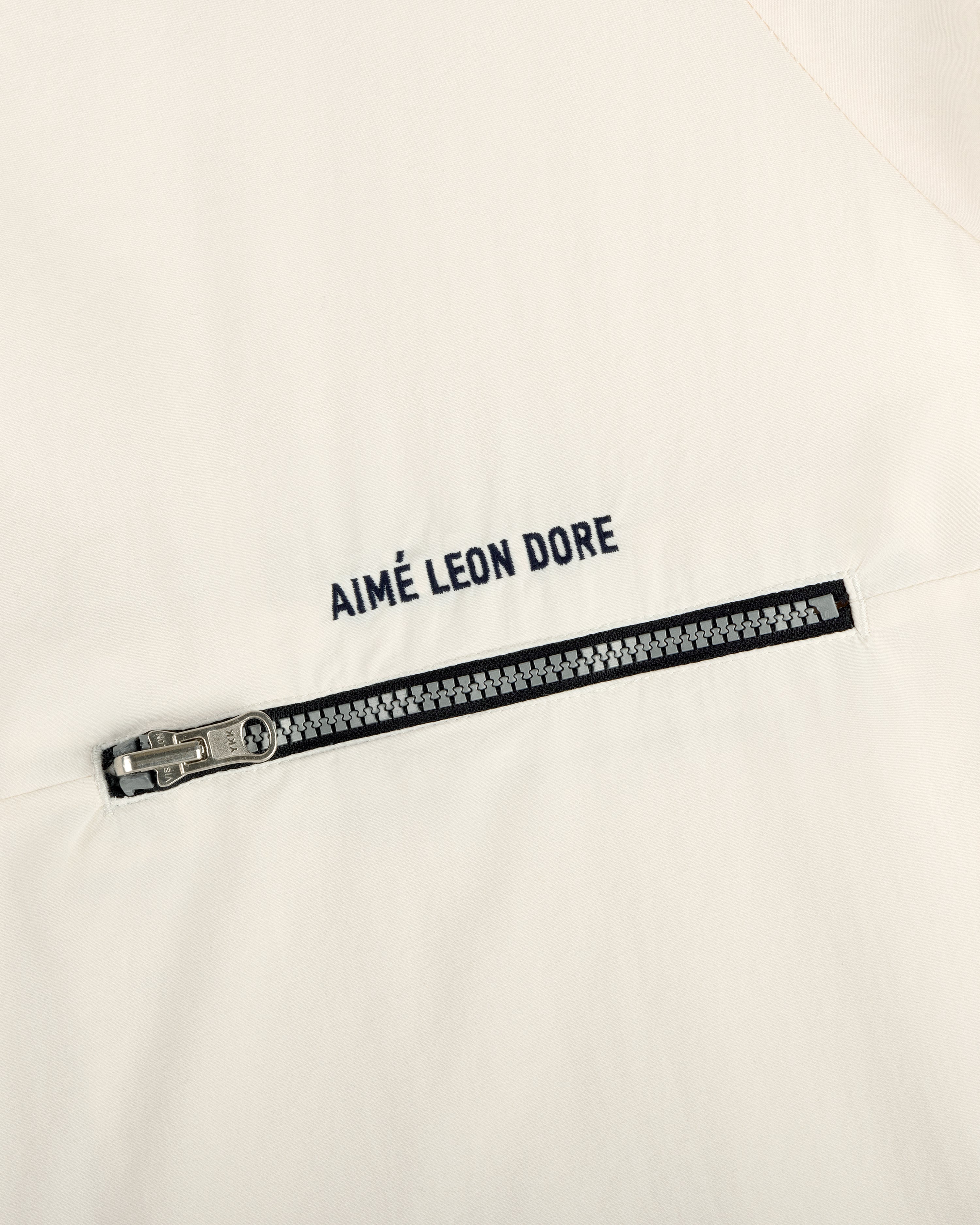 Close-up of an off-white Nylon Packable Windbreaker with a silver zipper and AIMÉ LEON DORE text above it.