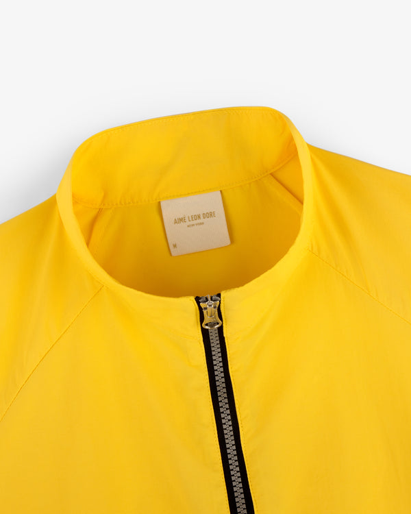 Close-up of a yellow Nylon Packable Windbreaker with a zipper and an Aimé Leon Dore label inside the collar.