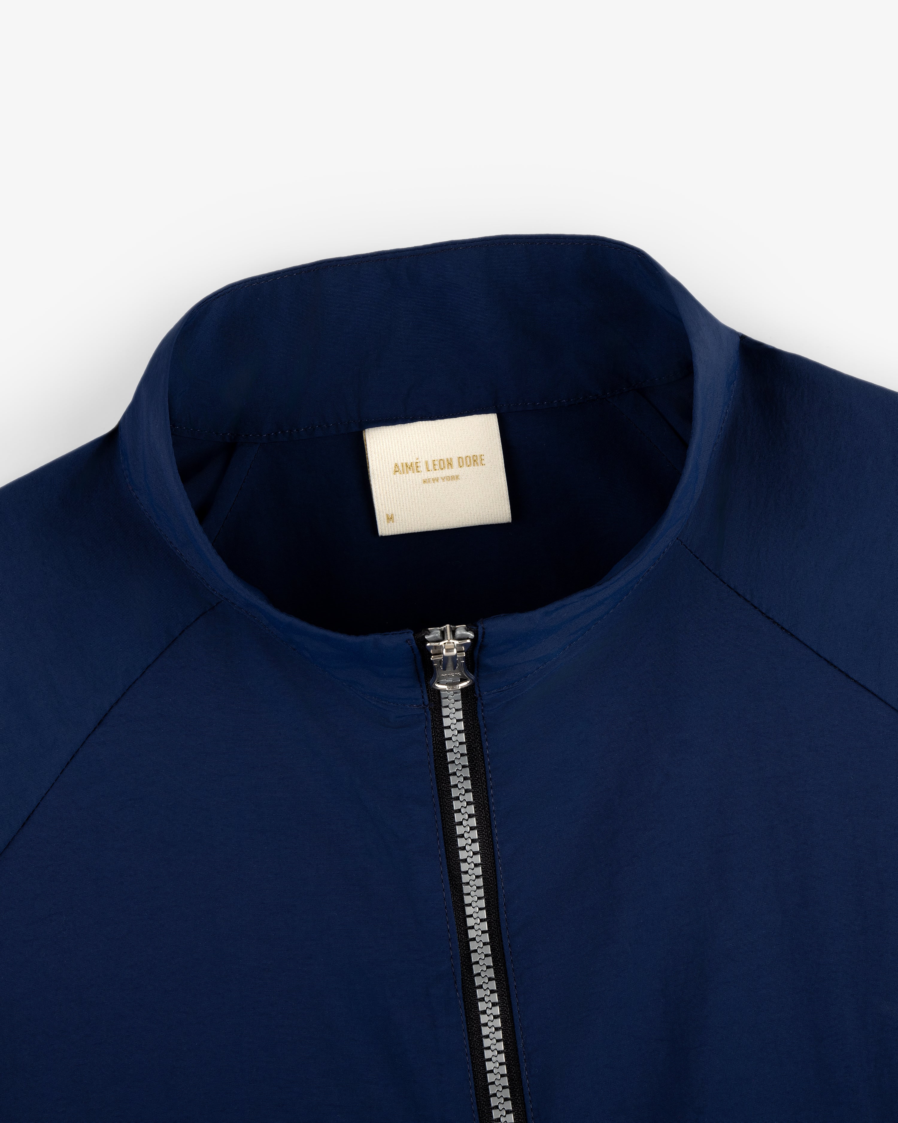 Close-up of a navy blue Nylon Packable Windbreaker with a white Aimé Leon Dore label inside the collar.