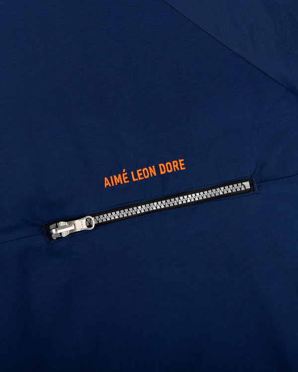 Close-up of the Nylon Packable Windbreaker in navy with a silver zipper and orange AIMÉ LEON DORE text above it.