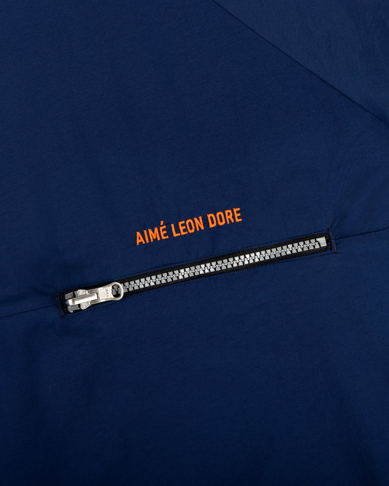 Close-up of the Nylon Packable Windbreaker in navy with a silver zipper and orange AIMÉ LEON DORE text above it.