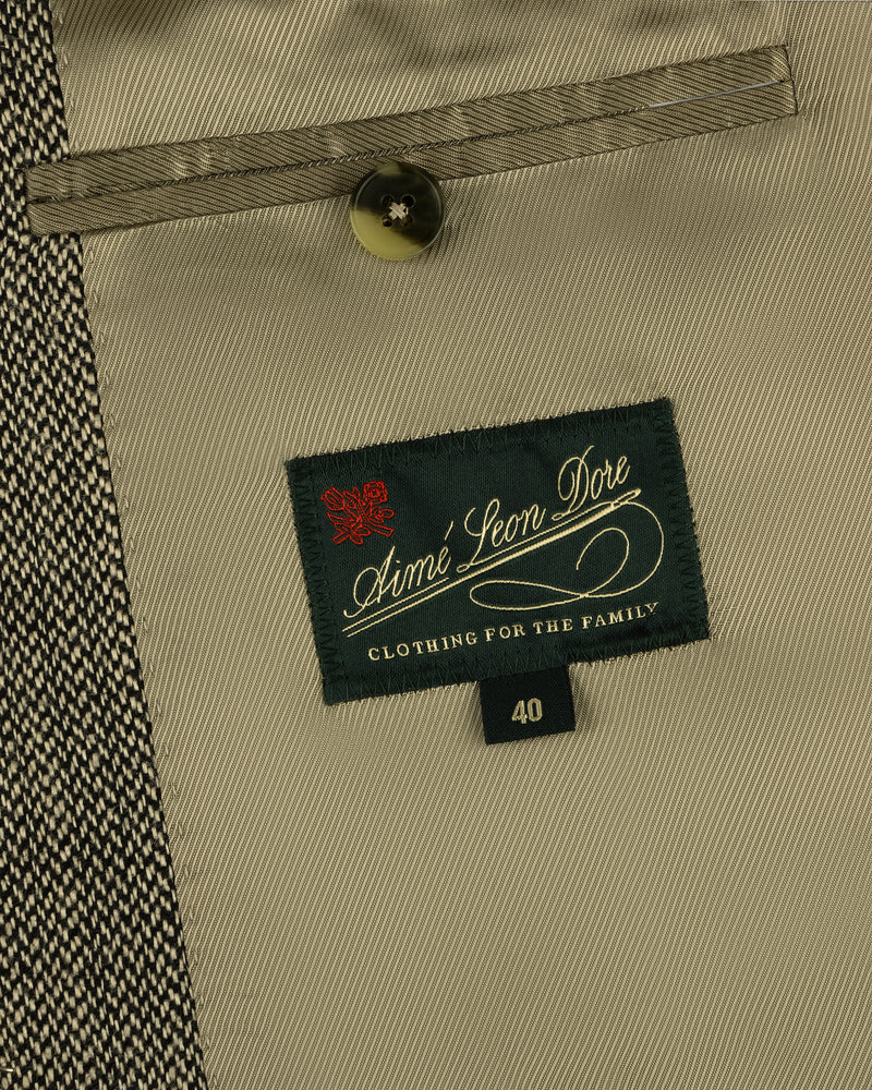 Close-up of a Single-Breasted Yarn Dyed Linen Suit Jacket label, button, and pocket on beige patterned fabric.