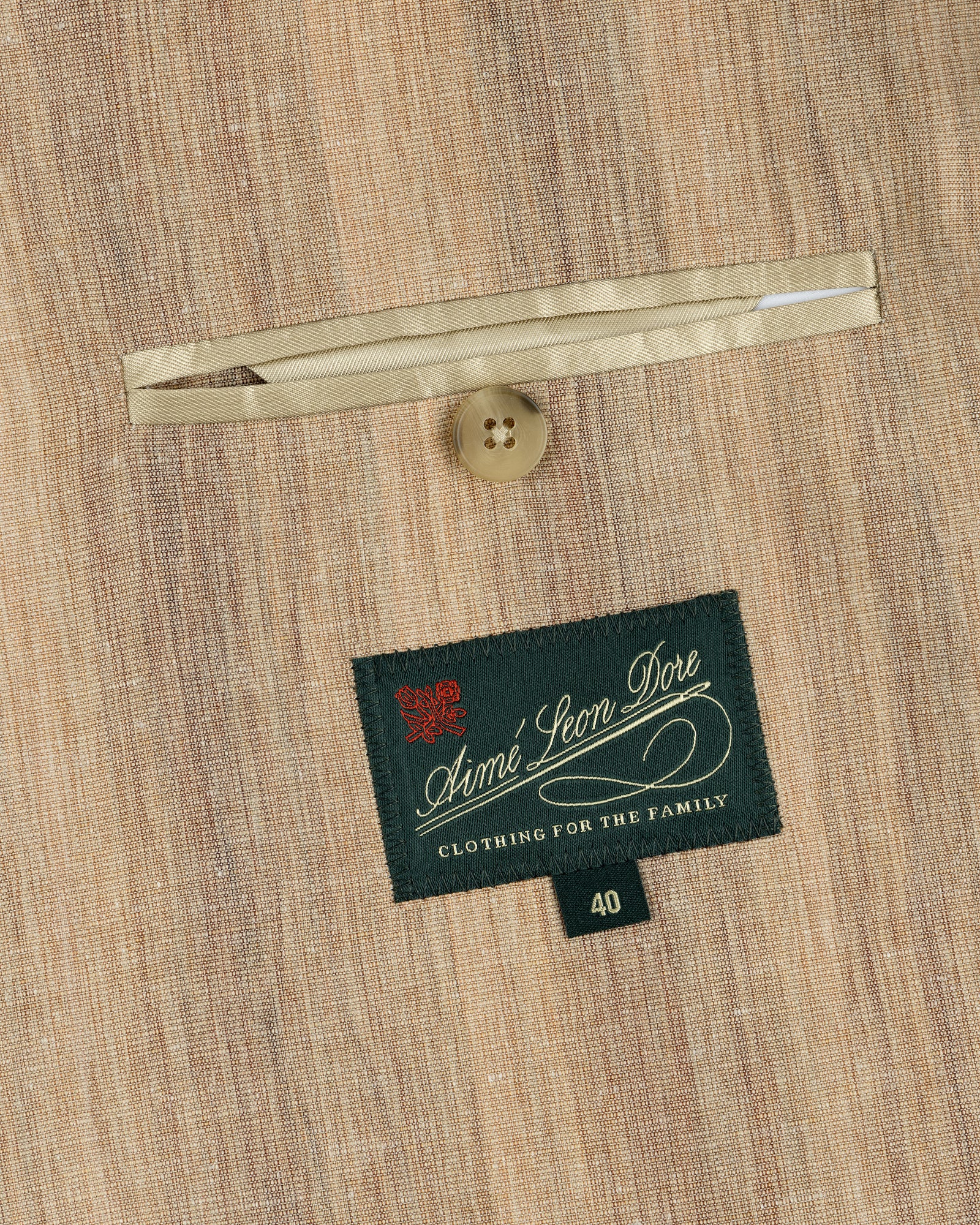 Close-up of a tan Single-Breasted Safari Suit Jacket pocket with a button and an Aimé Leon Dore label.