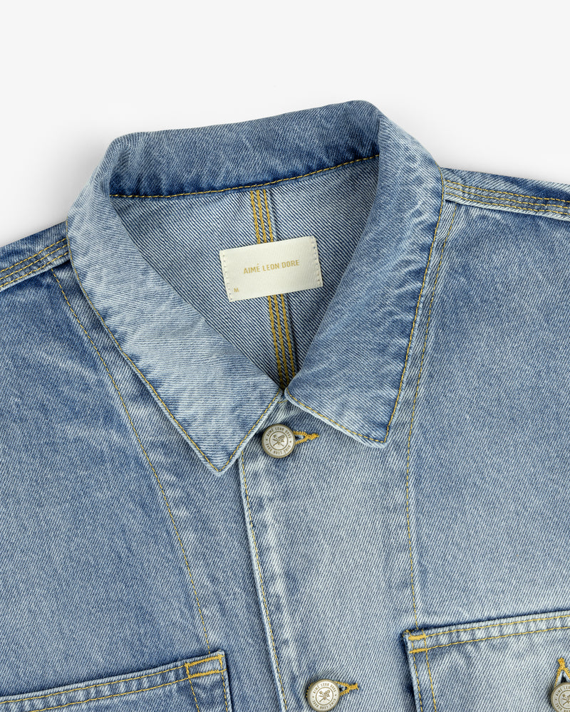 Close-up of a Denim Trucker Jacket in light blue with a collar, buttons, and visible inner label.