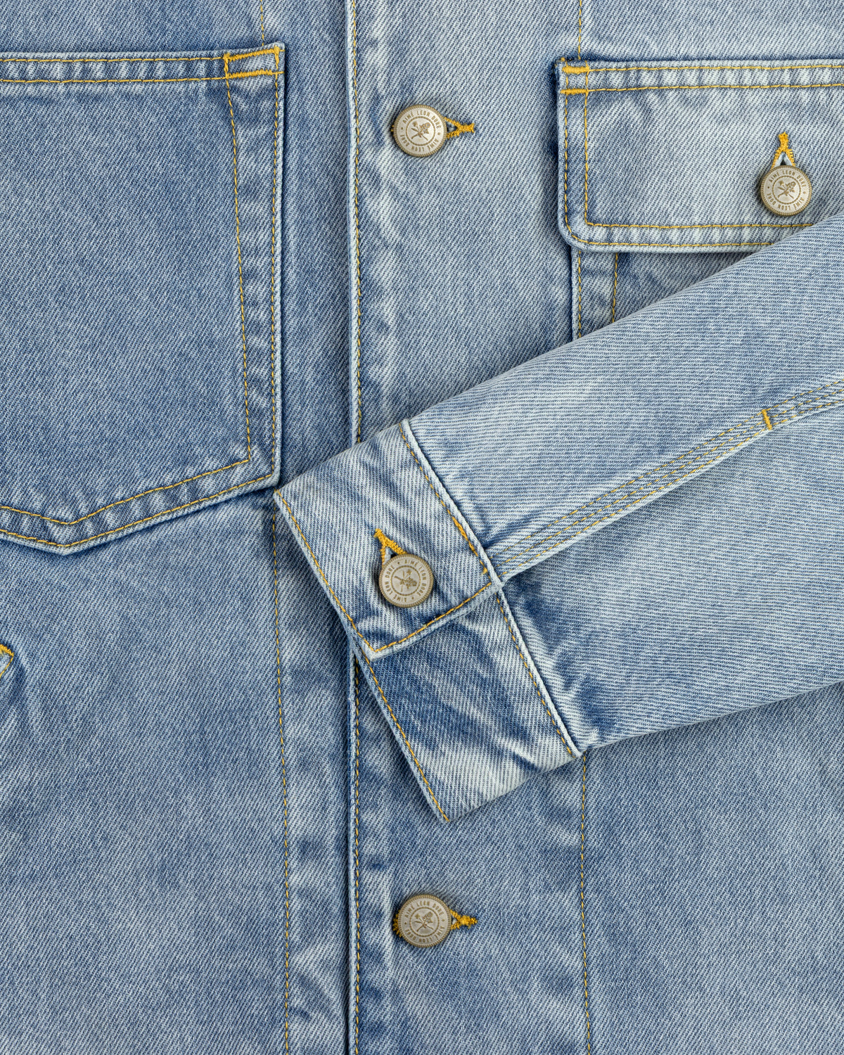 Close-up of a light blue Denim Trucker Jacket with visible buttons, stitching, and one sleeve crossing the front.