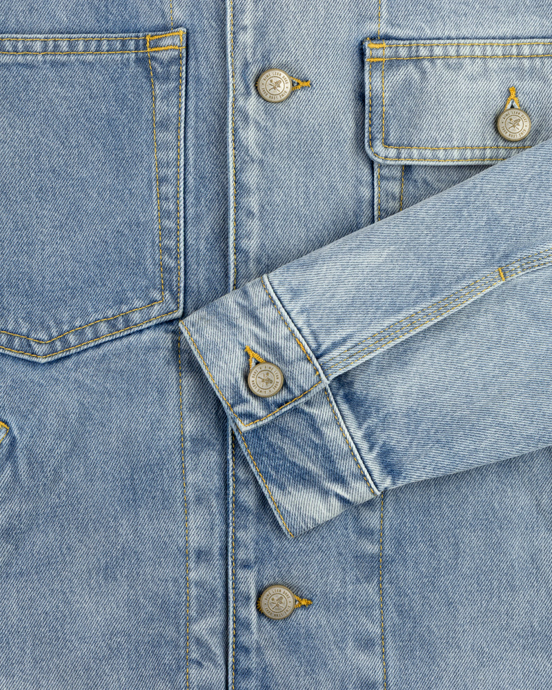 Close-up of a light blue Denim Trucker Jacket with visible buttons, stitching, and one sleeve crossing the front.