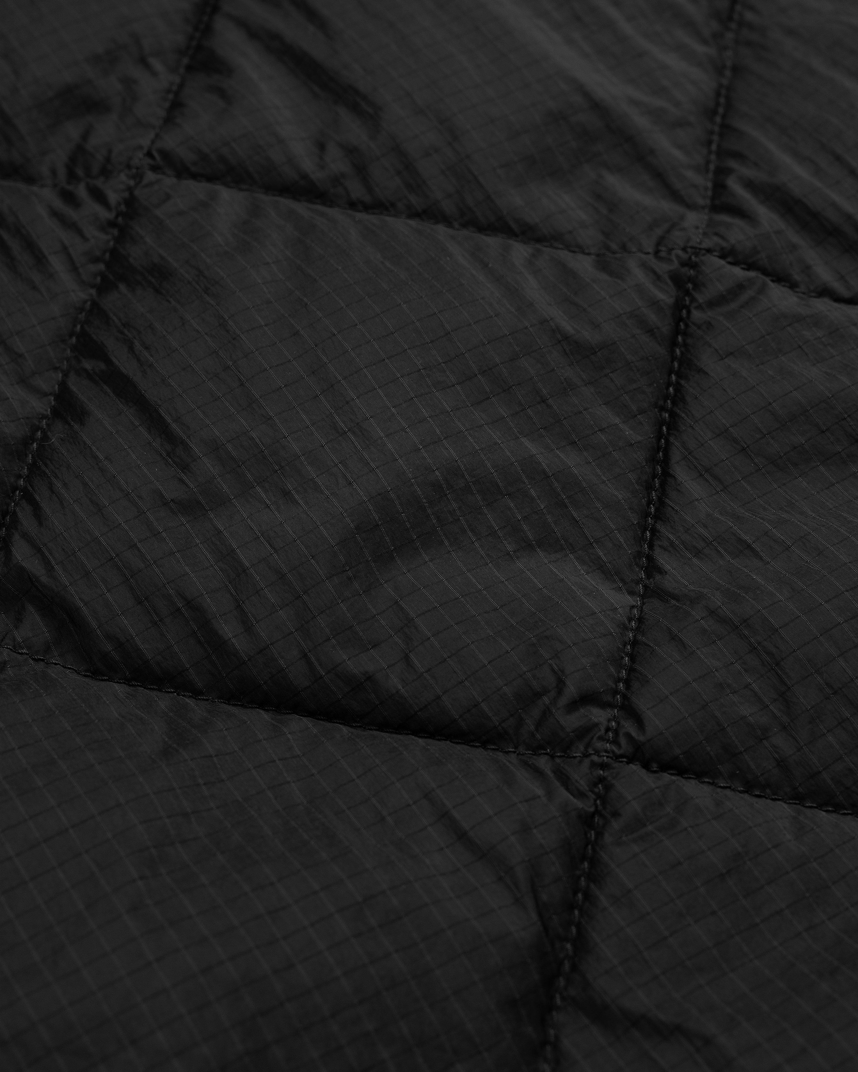 Close-up of the Nylon Quilted Unisphere Jacket's black quilted fabric with visible stitching and a subtle grid pattern.