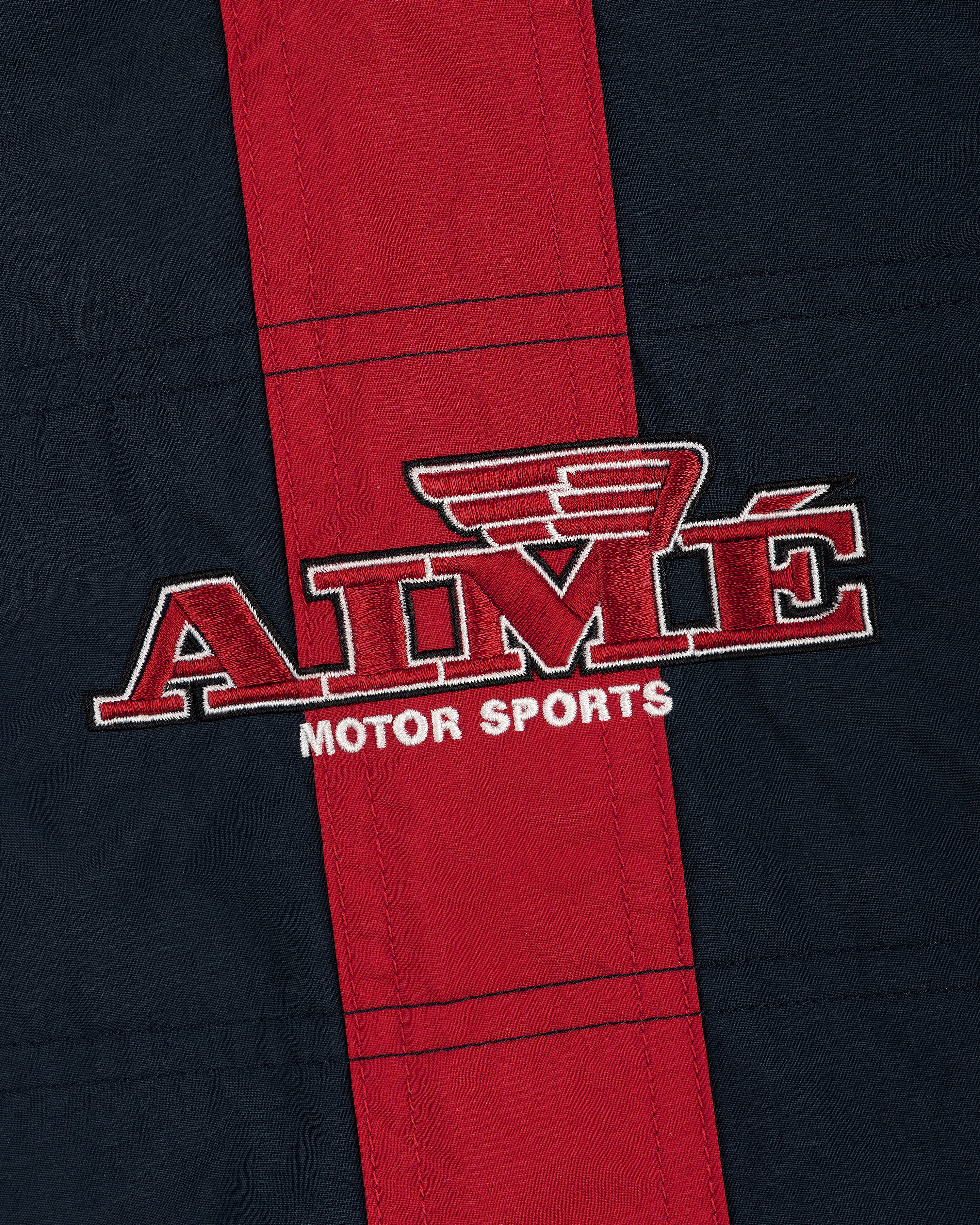 Close-up of AIMÉ MOTOR SPORTS logo embroidered on the red and navy Nylon Moto Jacket.
