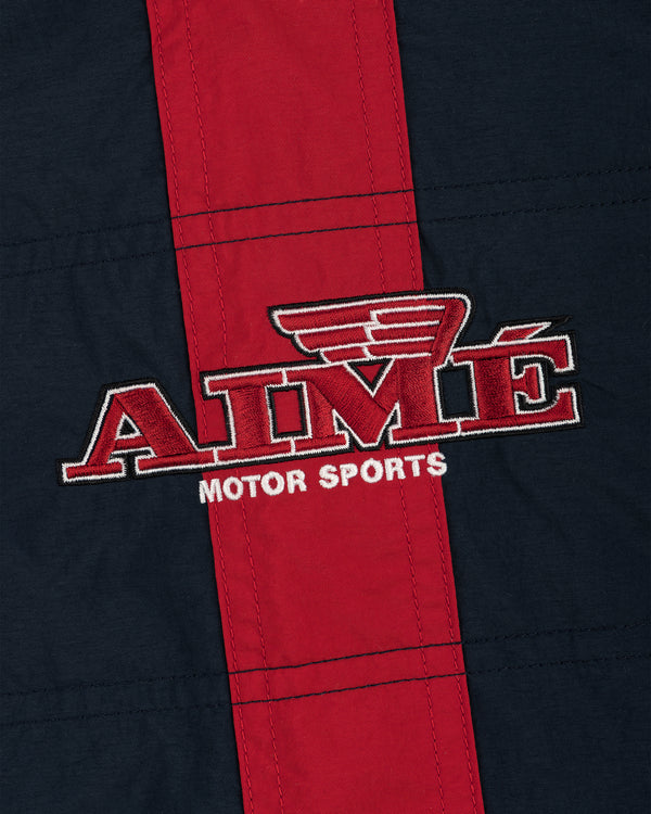 Close-up of AIMÉ MOTOR SPORTS logo embroidered on the red and navy Nylon Moto Jacket.