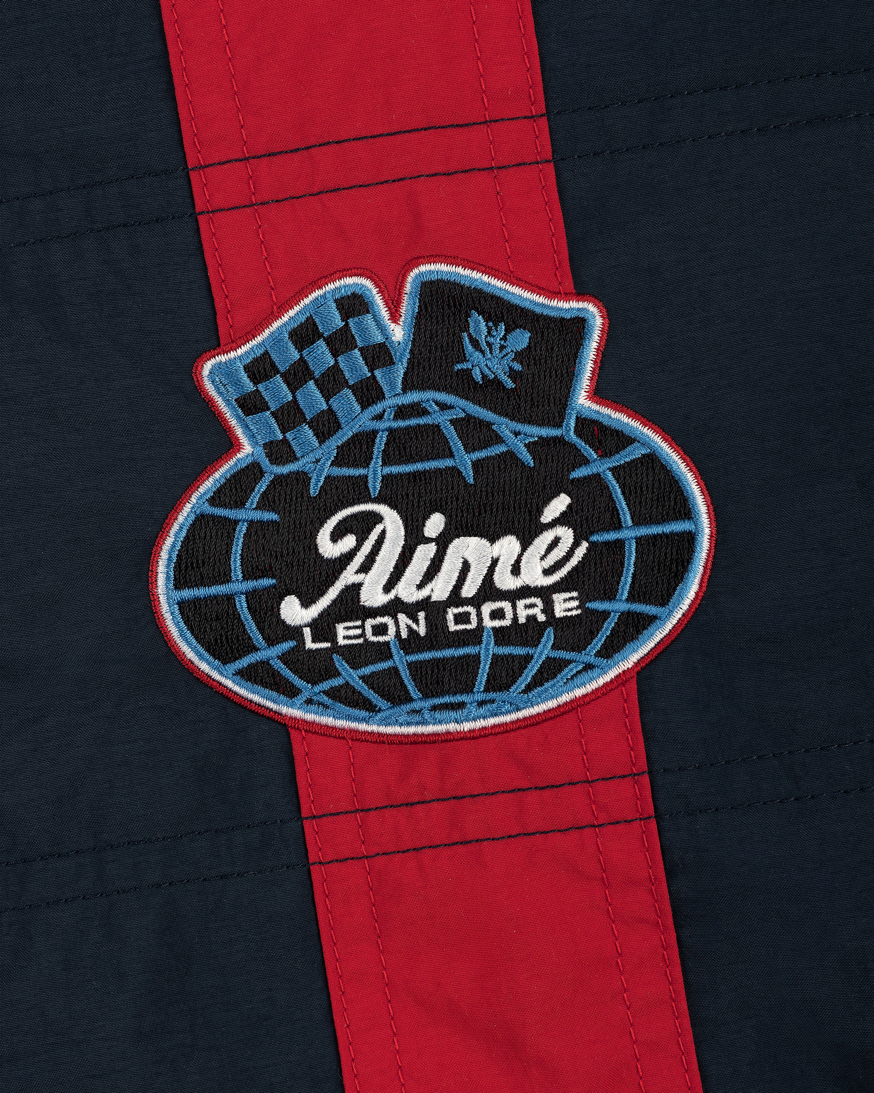 Nylon Moto Jacket in navy and red with an Aimé Leon Dore globe patch featuring a checkered flag and laurel emblem.