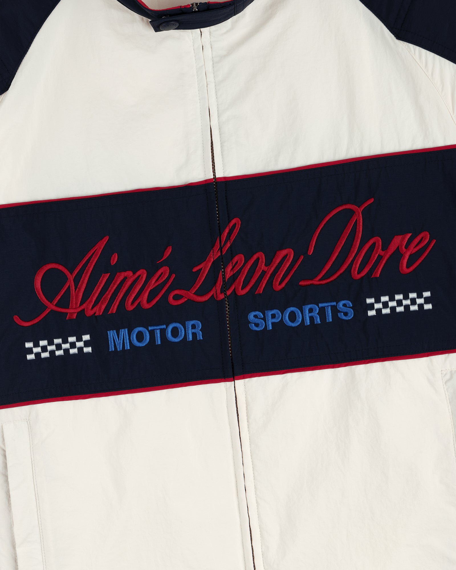 White Aimé Leon Dore Nylon Moto Jacket with MOTOR SPORTS and checkered flags on a navy chest panel.