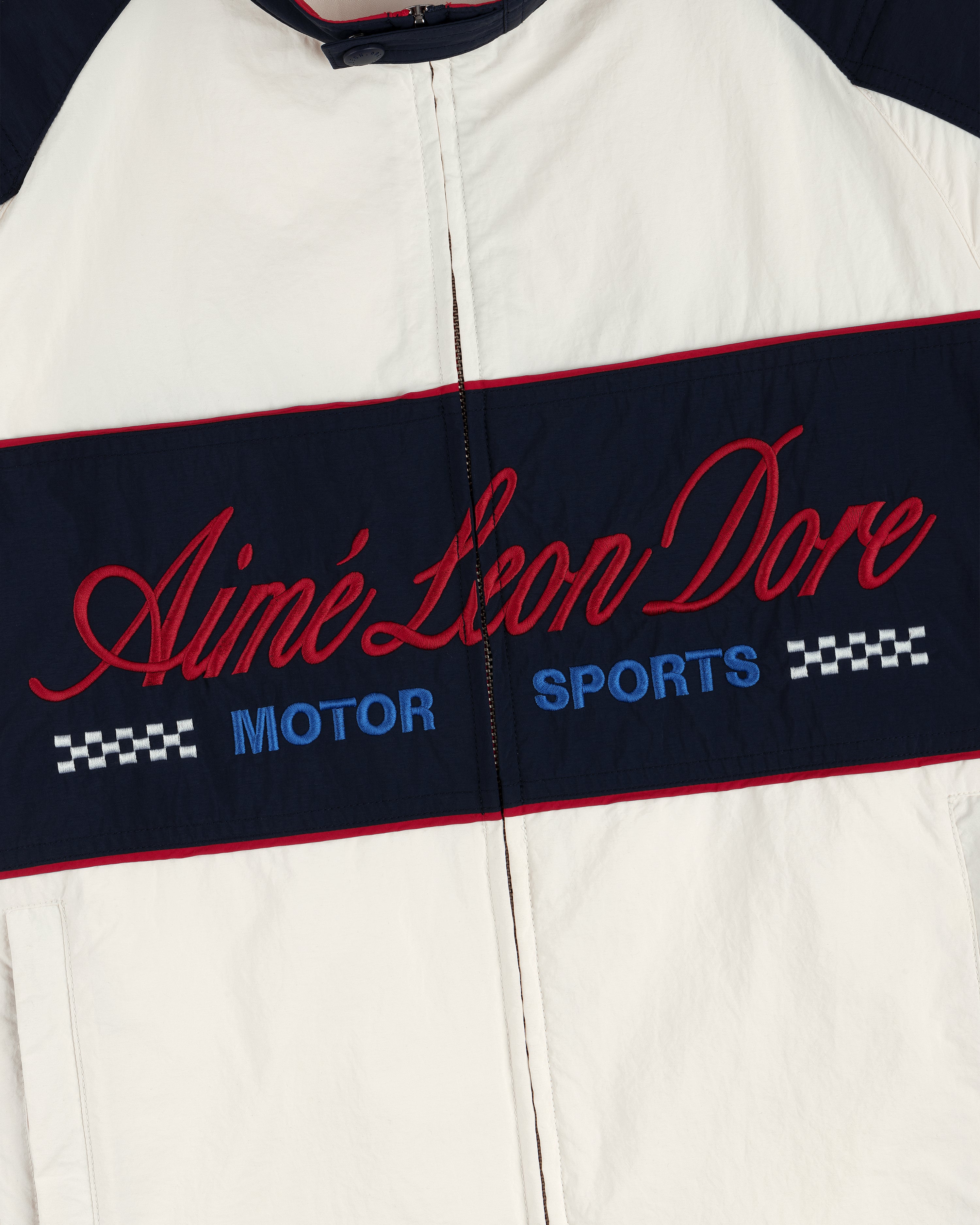 White Aimé Leon Dore Nylon Moto Jacket with MOTOR SPORTS and checkered flags on a navy chest panel.