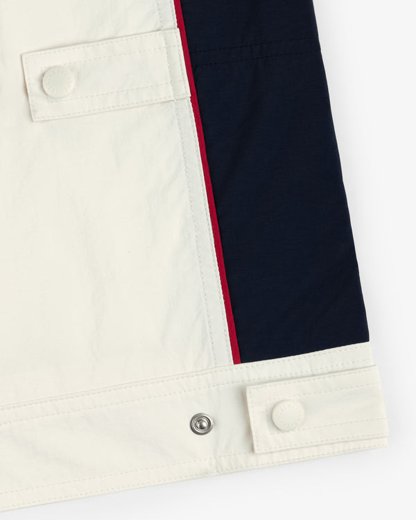 Close-up of the Nylon Moto Jacket hem with white and navy fabric, red stripe, and button tab details.