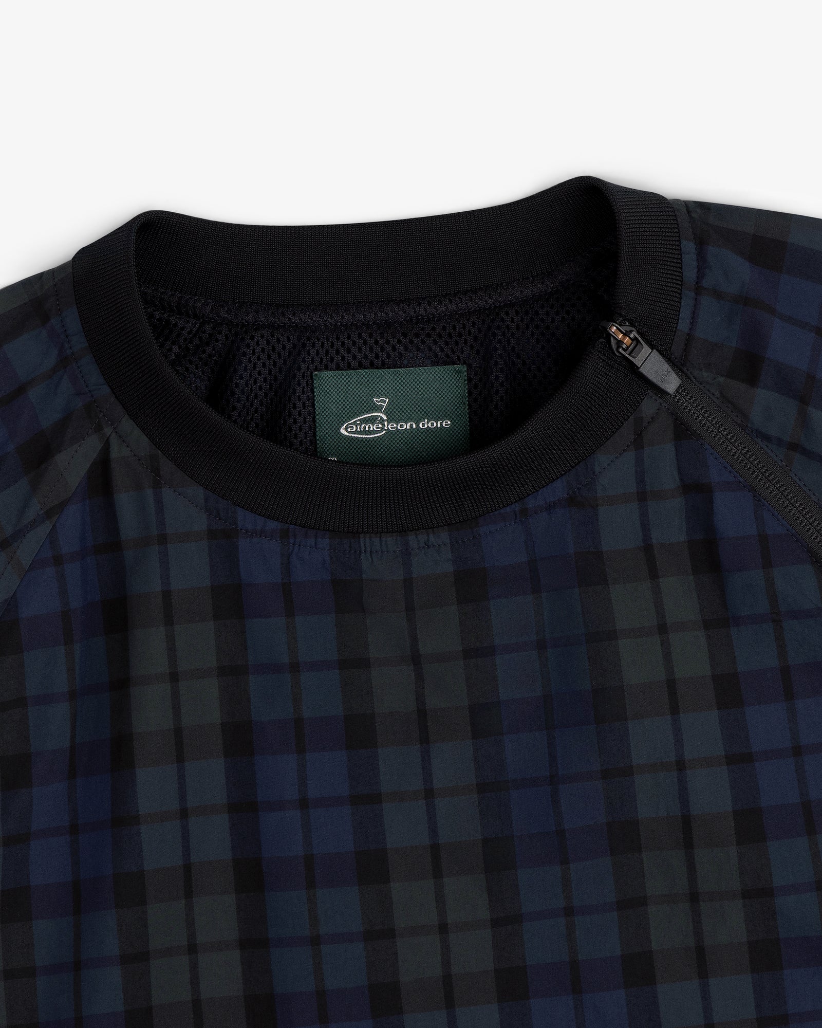 Close-up of the ALD Golf Blackwatch Pullover featuring navy and black plaid, a black collar, and a zip at the neckline.