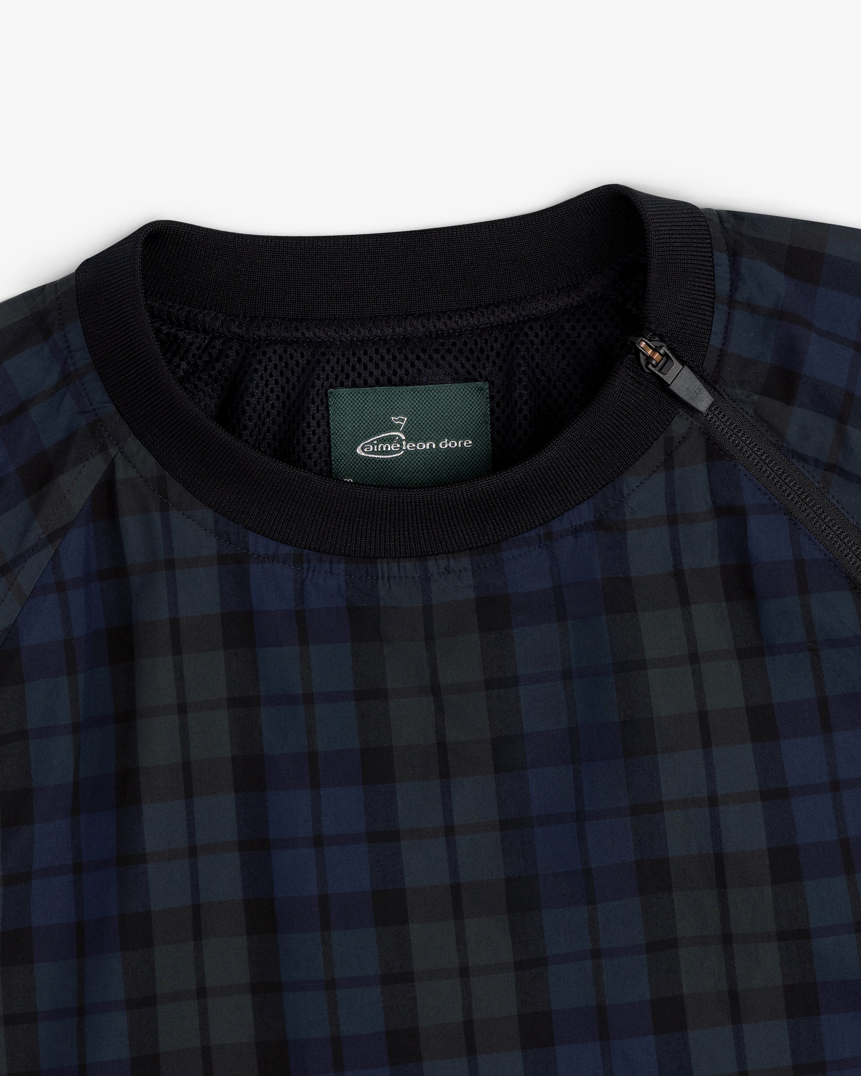 Close-up of the ALD Golf Blackwatch Pullover featuring navy and black plaid, a black collar, and a zip at the neckline.