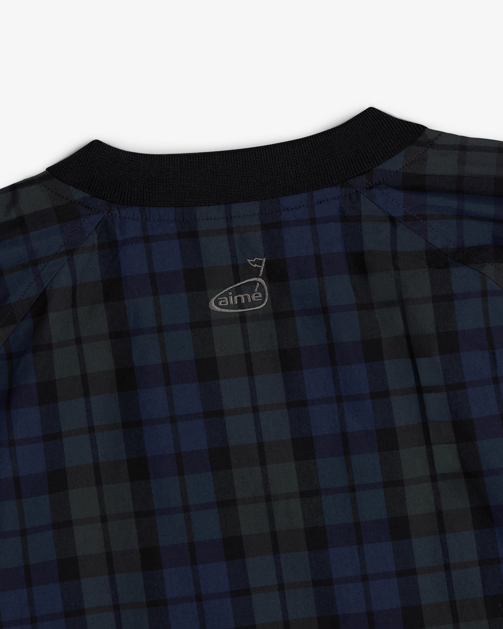 Close-up of the ALD Golf Blackwatch Pullover, a blue and black plaid shirt with a black collar and aime logo on the back.