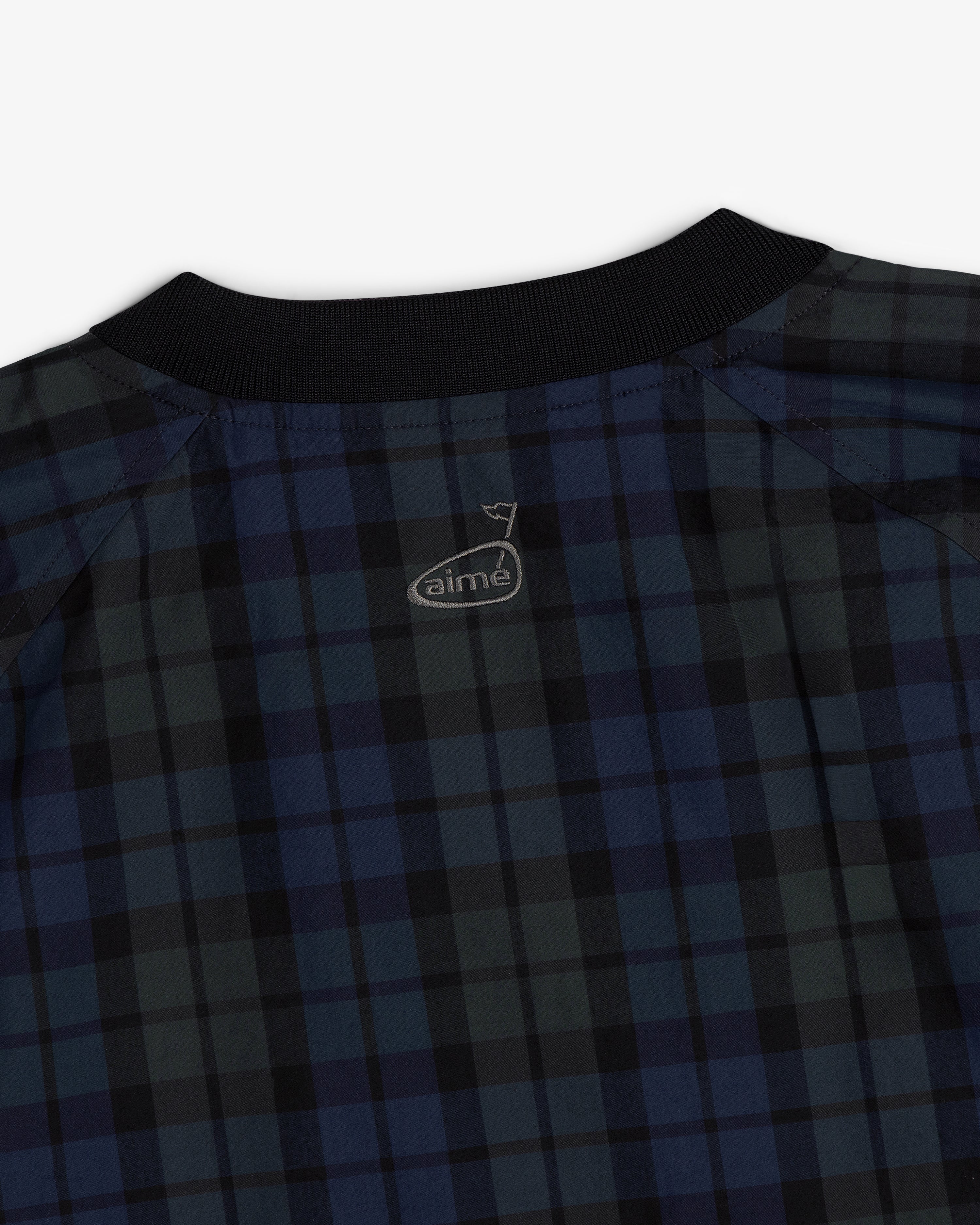 Close-up of the ALD Golf Blackwatch Pullover, a blue and black plaid shirt with a black collar and aime logo on the back.