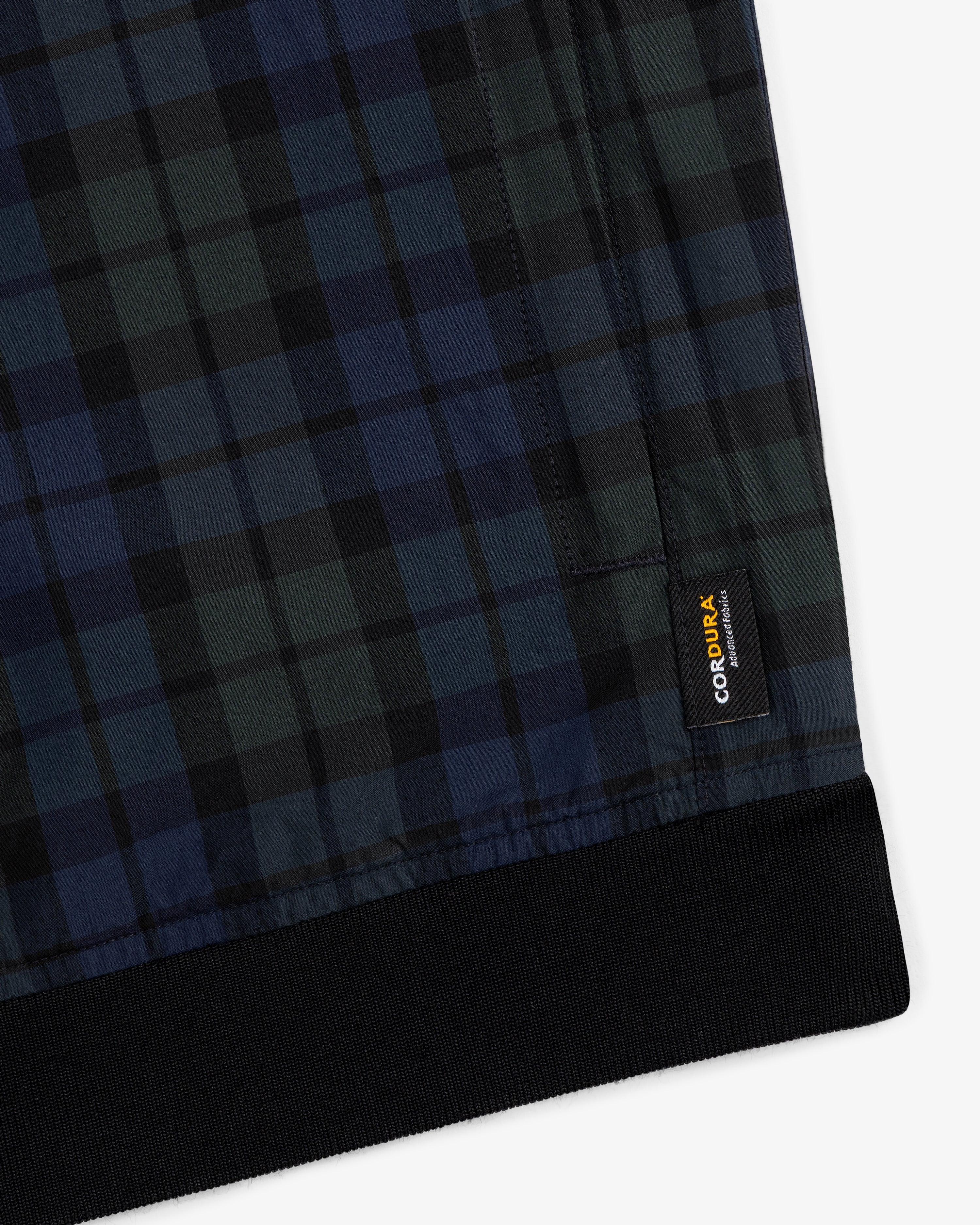 Close-up of ALD Golf Blackwatch Pullover featuring blue and green plaid with a black cuff and Cordura brand tag.
