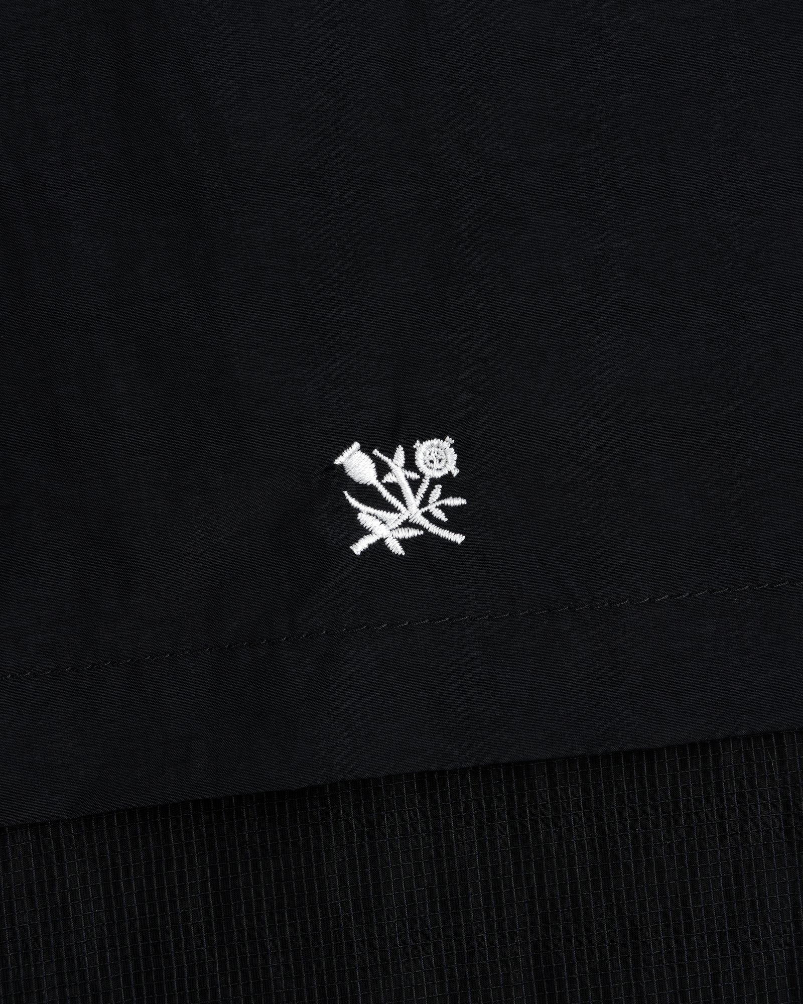 Small white embroidered flower near the hem of a black Nylon Track Jacket.