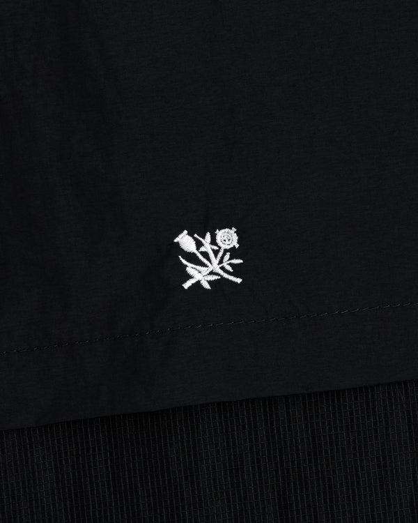 Small white embroidered flower near the hem of a black Nylon Track Jacket.