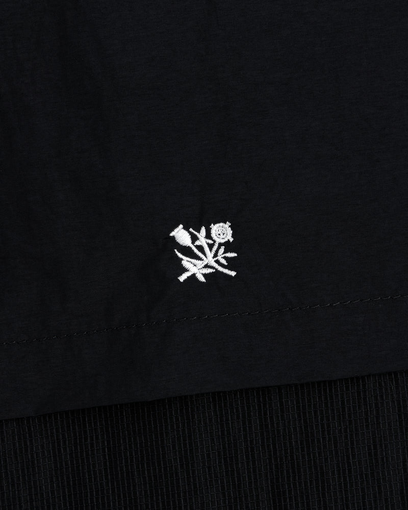 Small white embroidered flower near the hem of a black Nylon Track Jacket.