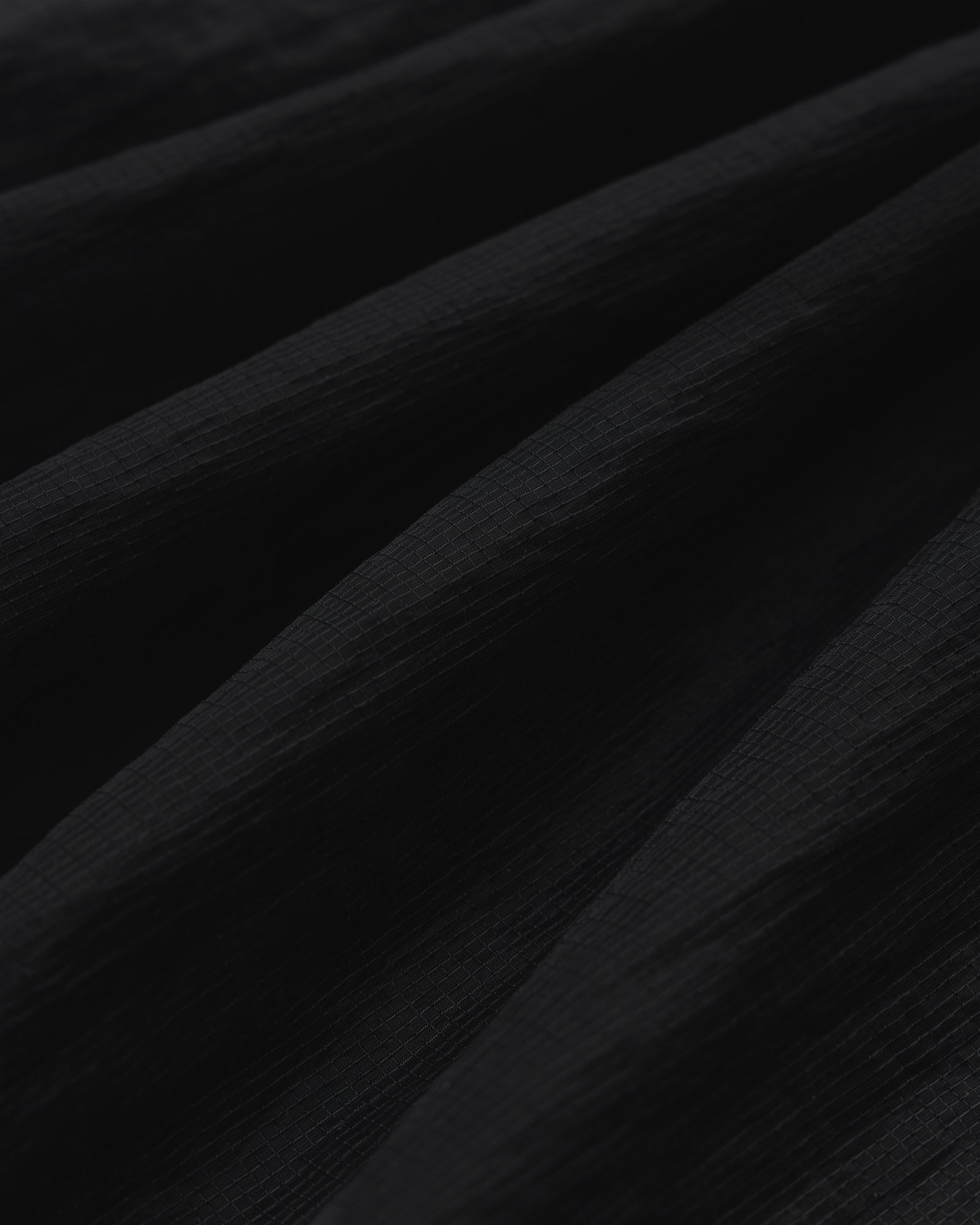 Close-up of black Nylon Track Jacket fabric with soft, diagonal folds creating shadows and depth.