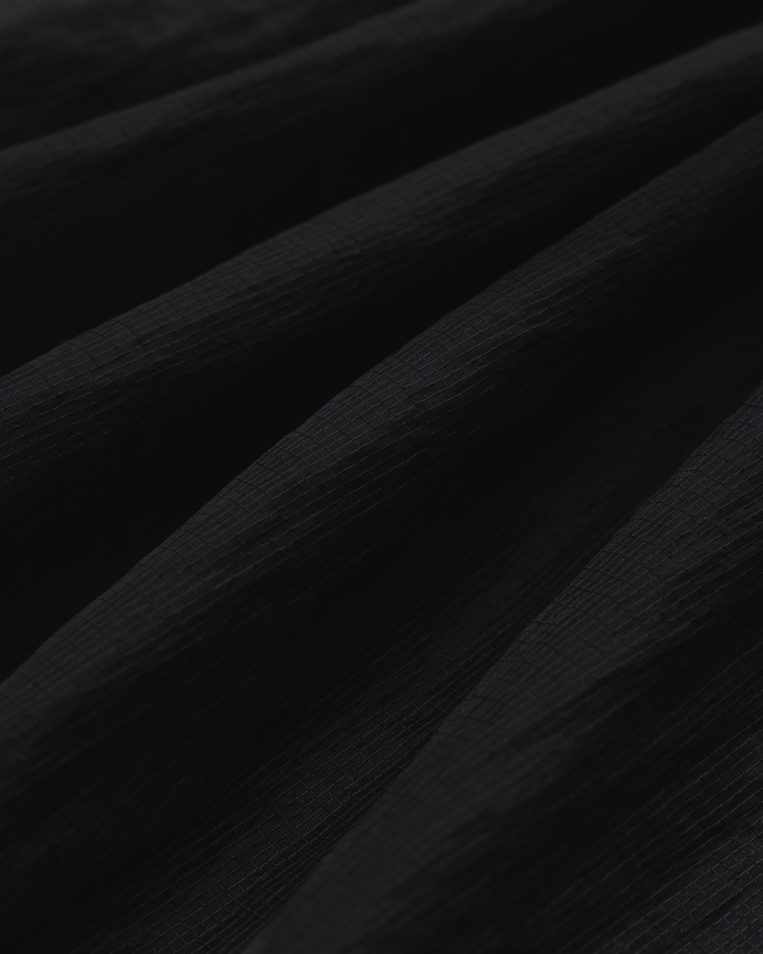 Close-up of black Nylon Track Jacket fabric with soft, diagonal folds creating shadows and depth.