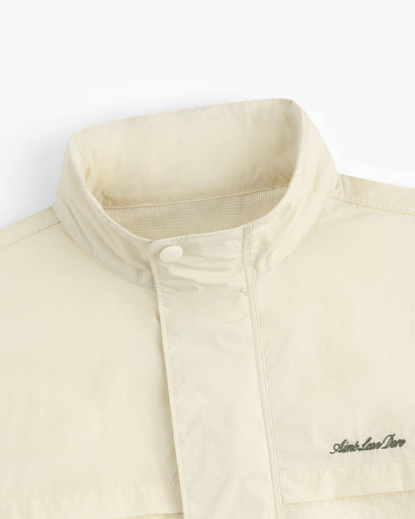 Close-up of the Nylon Track Jacket in cream with a high collar and Aimé Leon Dore logo on the chest.