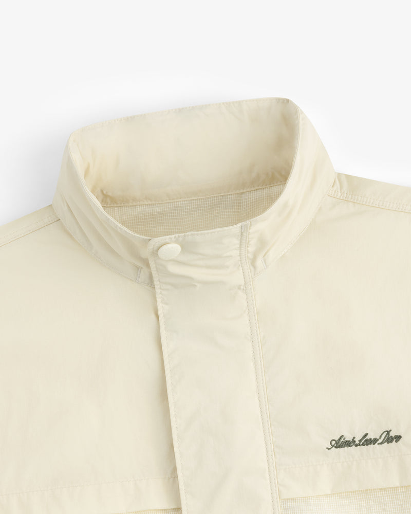 Close-up of the Nylon Track Jacket in cream with a high collar and Aimé Leon Dore logo on the chest.