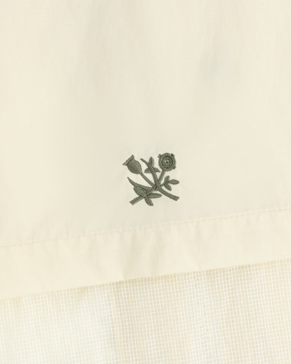 Embroidered green flower and stem motif on cream nylon track jacket with a subtle grid pattern below.