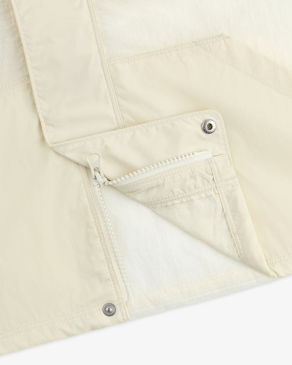 Close-up of the Nylon Track Jacket, cream-colored with a white zipper, snap buttons, and part of the pocket and lapel.