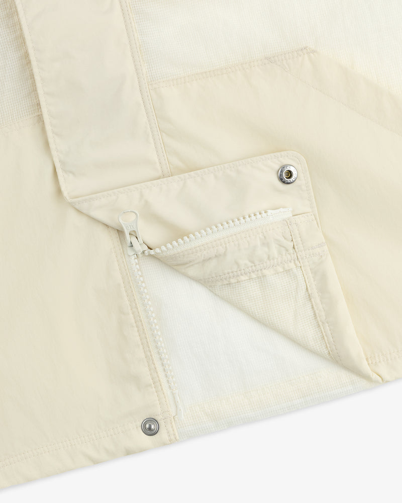 Close-up of the Nylon Track Jacket, cream-colored with a white zipper, snap buttons, and part of the pocket and lapel.