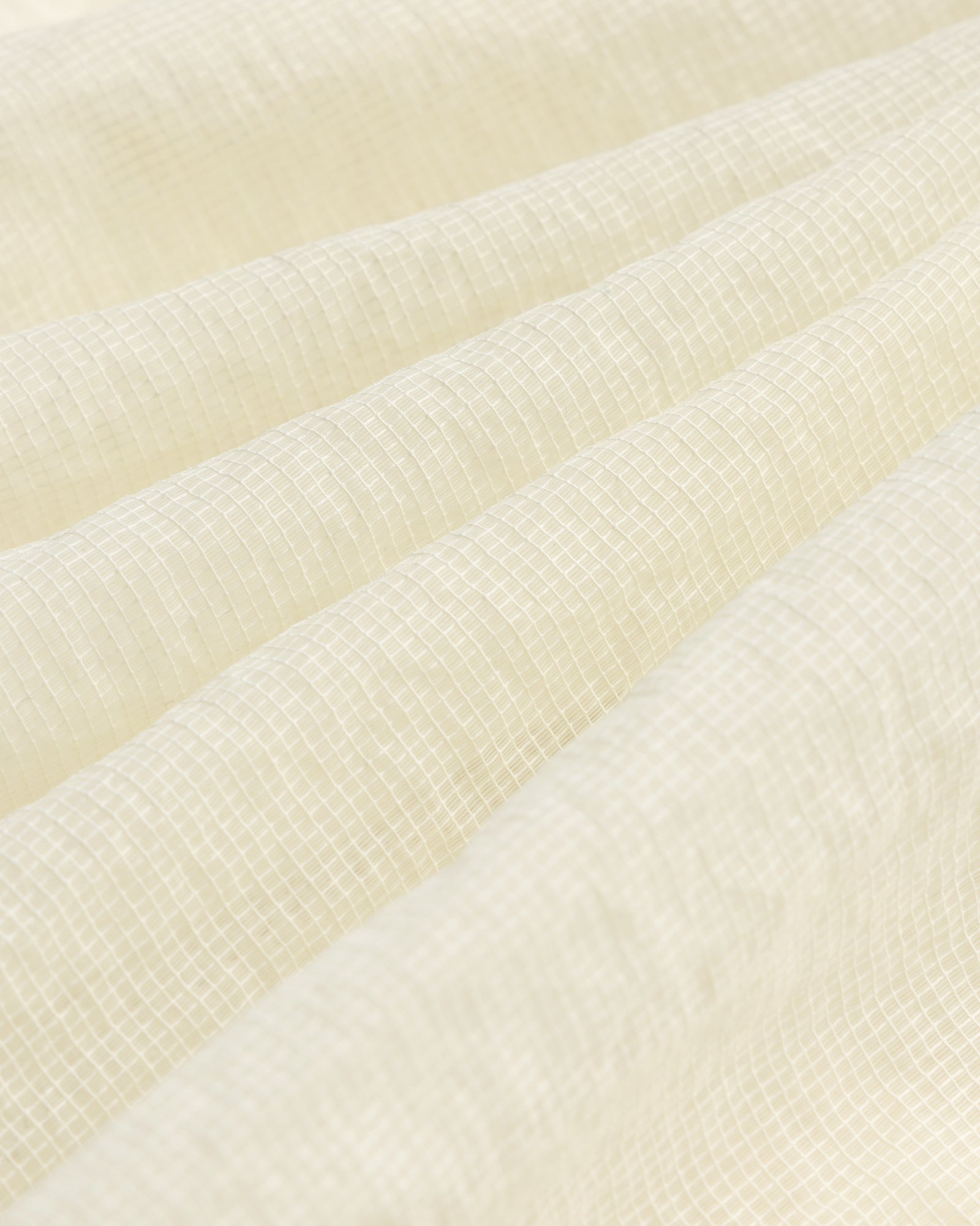 Close-up of cream-colored textured fabric with a subtle grid on the Nylon Track Jacket and gentle folds.