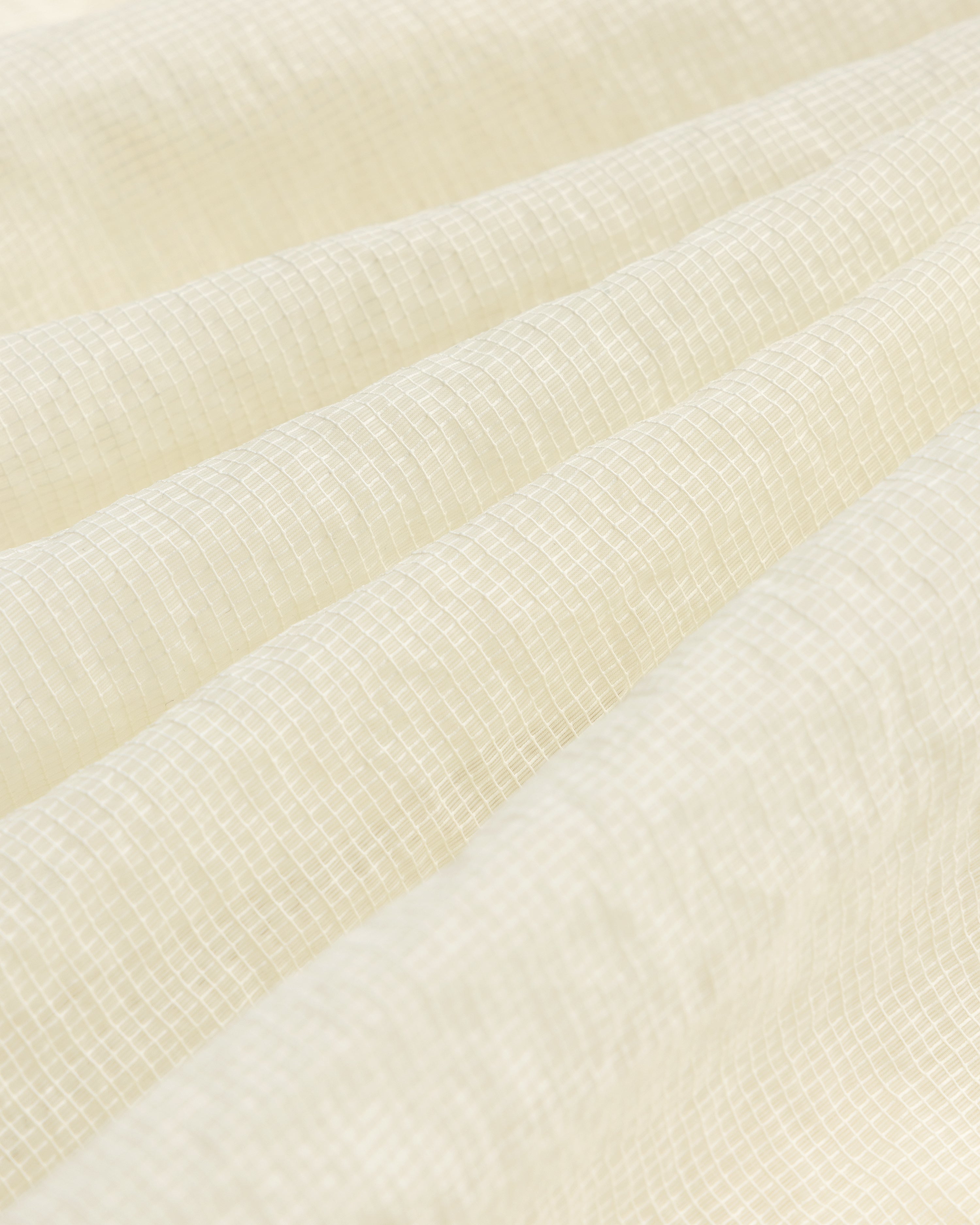 Close-up of cream-colored textured fabric with a subtle grid on the Nylon Track Jacket and gentle folds.