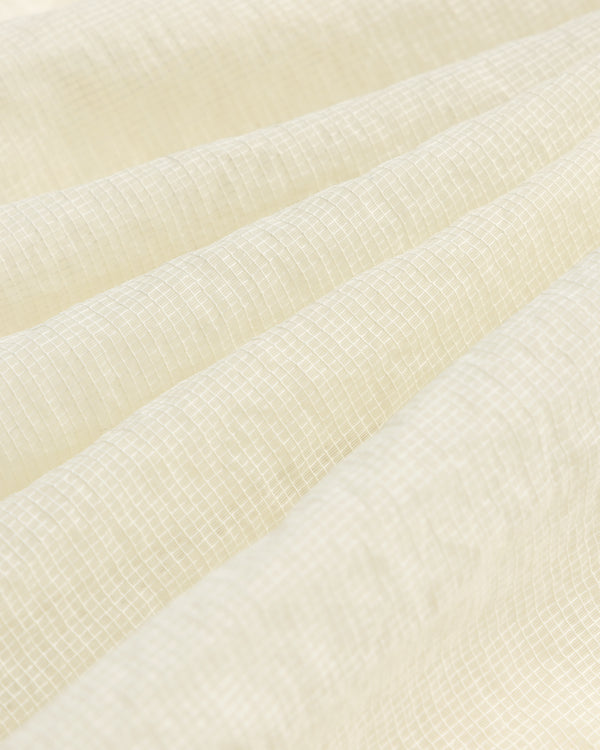 Close-up of cream-colored textured fabric with a subtle grid on the Nylon Track Jacket and gentle folds.