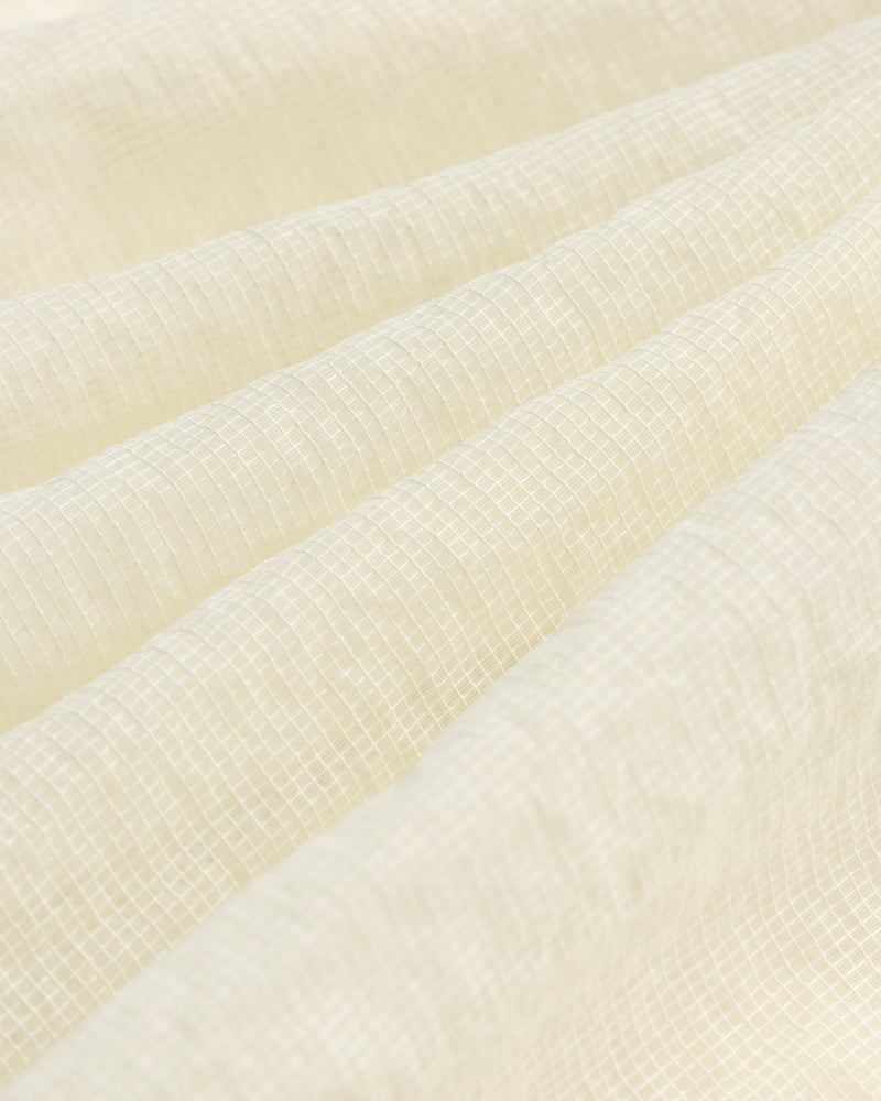 Close-up of cream-colored textured fabric with a subtle grid on the Nylon Track Jacket and gentle folds.