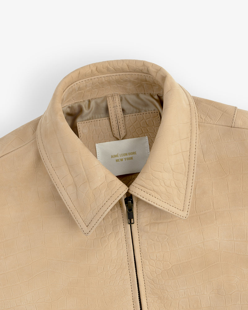 Close-up of a beige Croc-Embossed Nubuck Bomber Jacket with collar and zipper, label reads AIME LEON DORE NEW YORK.