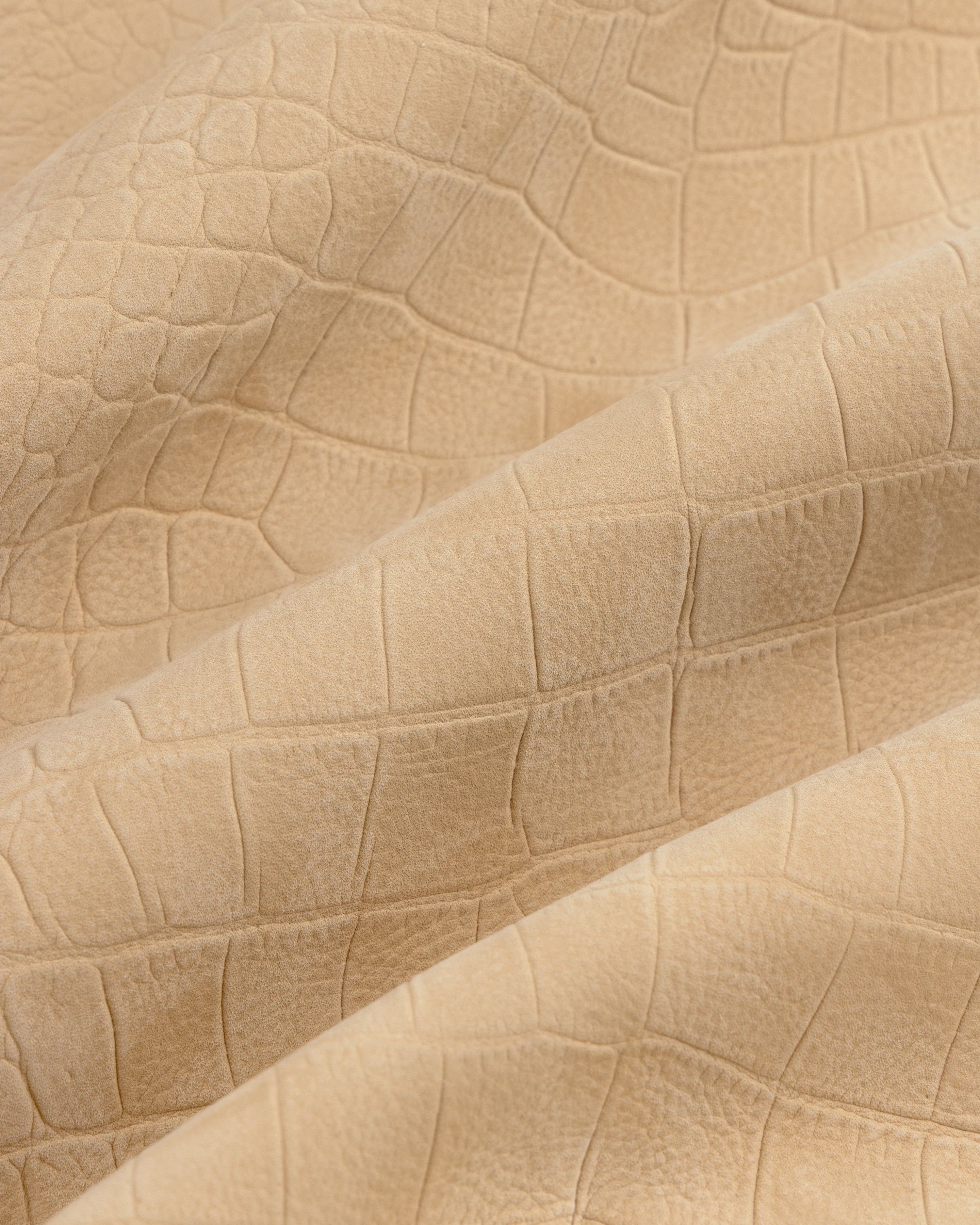 Close-up of Croc-Embossed Nubuck Bomber Jacket’s beige, matte, crocodile-patterned textured fabric with gentle folds.