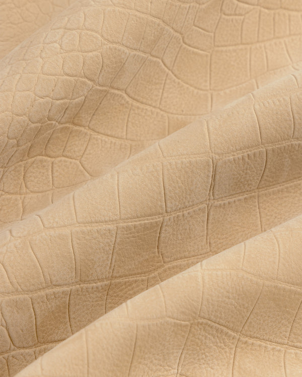 Close-up of Croc-Embossed Nubuck Bomber Jacket’s beige, matte, crocodile-patterned textured fabric with gentle folds.