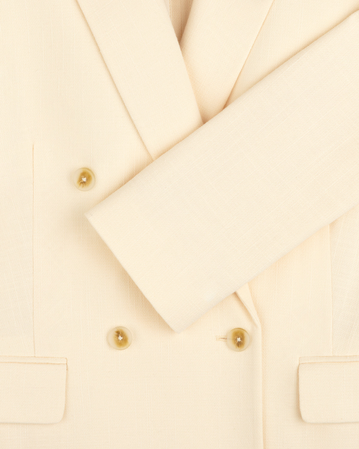 Close-up of the Double-Breasted Unconstructed Blazer in cream with double-breasted buttons and one sleeve folded across.