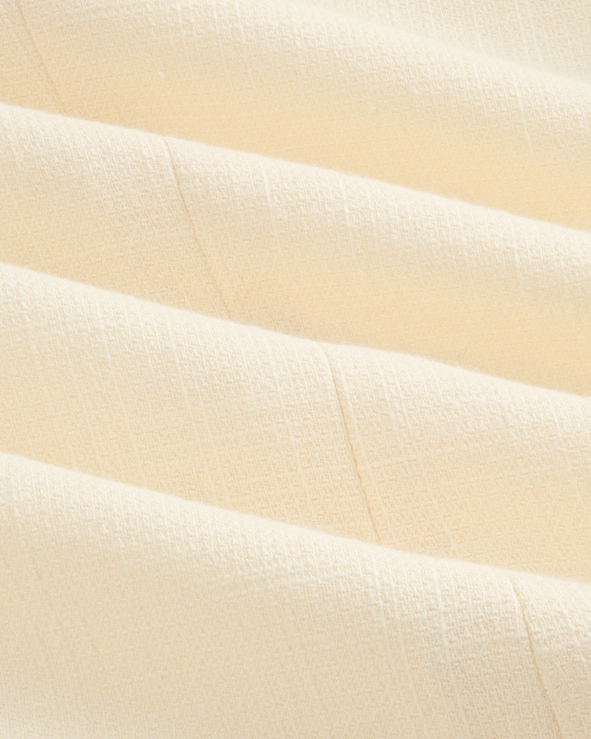 Close-up of cream-colored, textured fabric with soft folds on the Double-Breasted Unconstructed Blazer.
