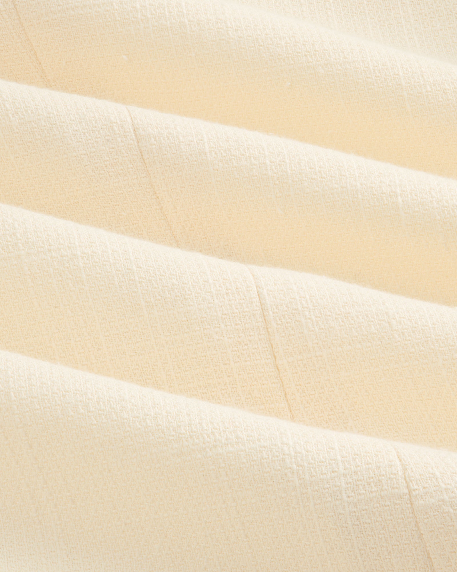 Close-up of cream-colored, textured fabric with soft folds on the Double-Breasted Unconstructed Blazer.