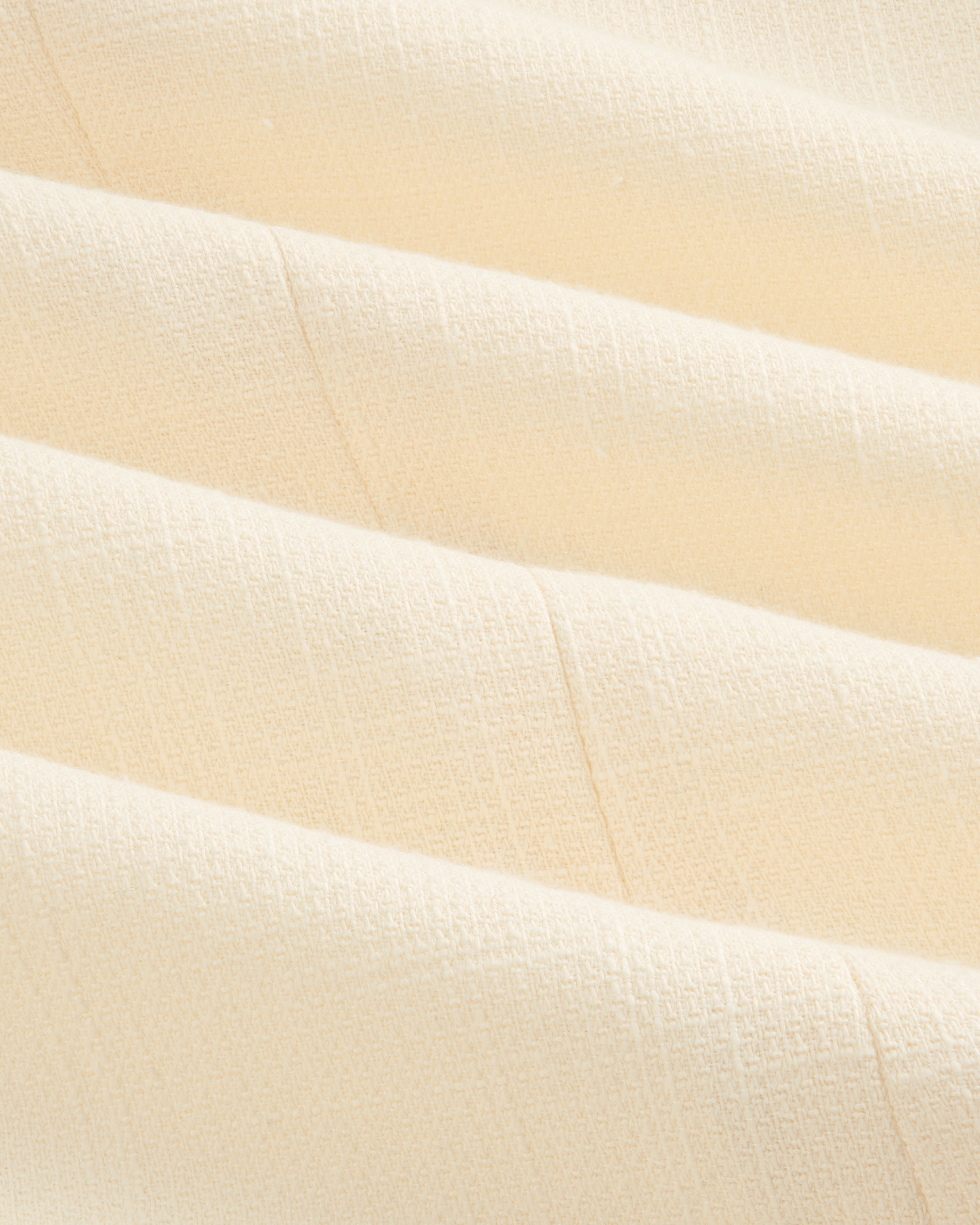 Close-up of cream-colored, textured fabric with soft folds on the Double-Breasted Unconstructed Blazer.