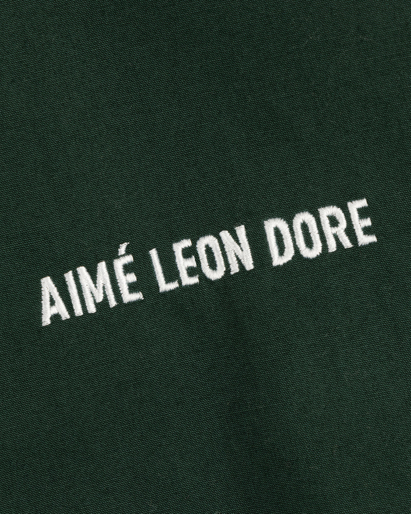 White "AIMÉ LEON DORE" text embroidered on dark green Micro Logo Lightweight Jacket, shown at a diagonal angle.