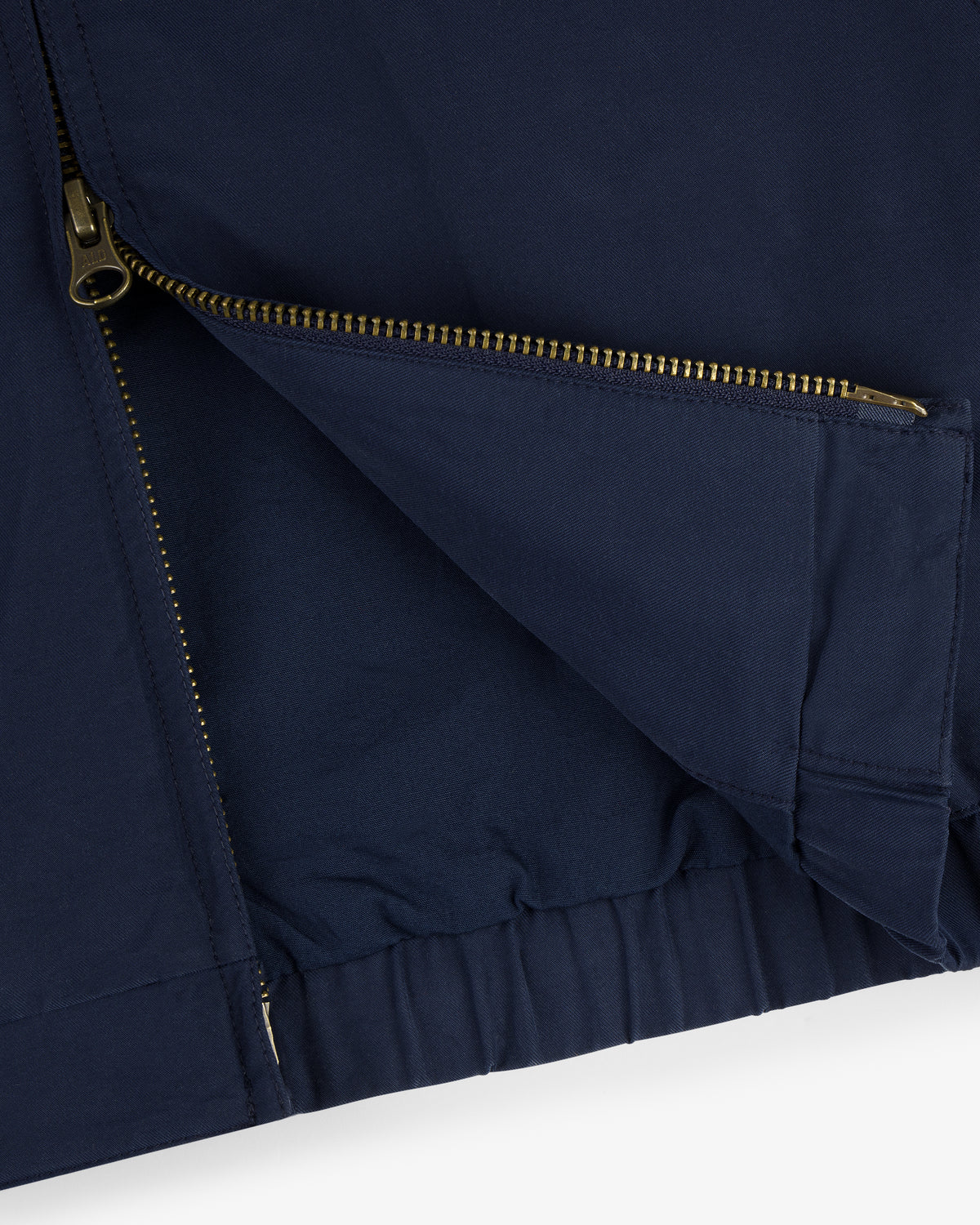Close-up of the Crest Casual Jacket in navy, featuring a gold zipper partially unzipped and elastic hem detail.